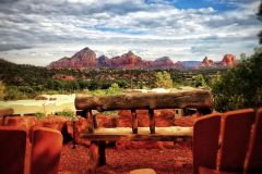 Wooden bench and chairs with blue sky filled with clouds in front of forest and mountains in background near Arabella Hotel Sedona in Sedona, AZ