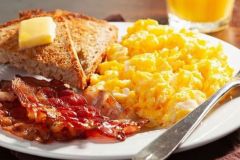 Plate with scrambled eggs, bacon and toast with butter on it near fork and glass of orange juice at Arabella Hotel Sedona in Sedona, AZ