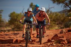 Three people on bicycles riding over rocks near trees in desert near Arabella Hotel Sedona in Sedona, AZ