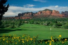 Golf course green with white flag sticking up near sand trap and water with mountains and trees and yellow flowers in background near Arabella Hotel Sedona in Sedona, AZ