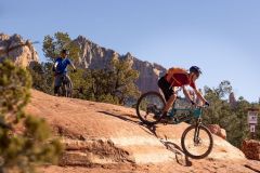 Two men mountain biking on rock surface near trees with red rock mountains in background near Arabella Hotel Sedona in Sedona, AZ