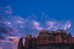 View to a red rock formation in the background and trees, bushes and cactuses in the foreground. Location is near Sedona, Arizona. Cathedral Rock Twilight.