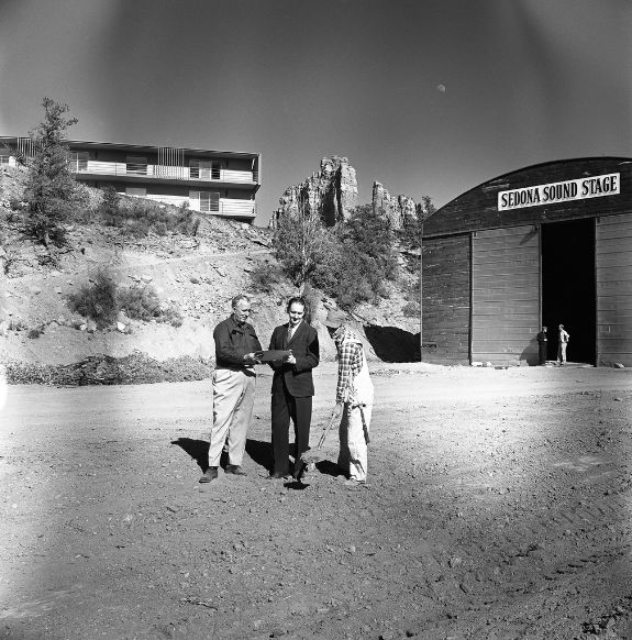 Black and white photo of three people shaking hands near Sedona Sound Stage in front of hotel and desert foliage with mountain in background near Arabella Hotel Sedona in Sedona, AZ