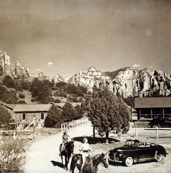 Black and white photo of two people on horseback in front of antique car with mountains and wooden houses in background near Arabella Hotel Sedona in Sedona, AZ