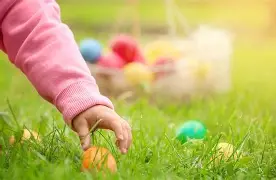 At Arabella Sedona, a child in a pink sleeve picks up a colorful Easter egg from the grass, with more eggs and a basket softly blurred behind.
