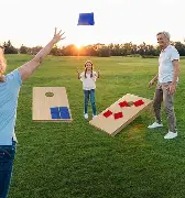Three people play cornhole on the grassy field at Arabella Sedona during sunset, tossing bean bags toward wooden boards with holes.