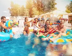 Five friends laugh and splash water on colorful floats at a sunny Arabella Sedona pool party, relaxing together and enjoying the vibrant outdoor scene.