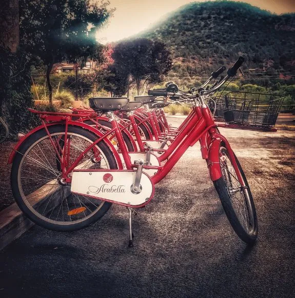 A line of red bicycles parked in front of trees with mountains in the background near Arabella Hotel Sedona in Sedona, AZ