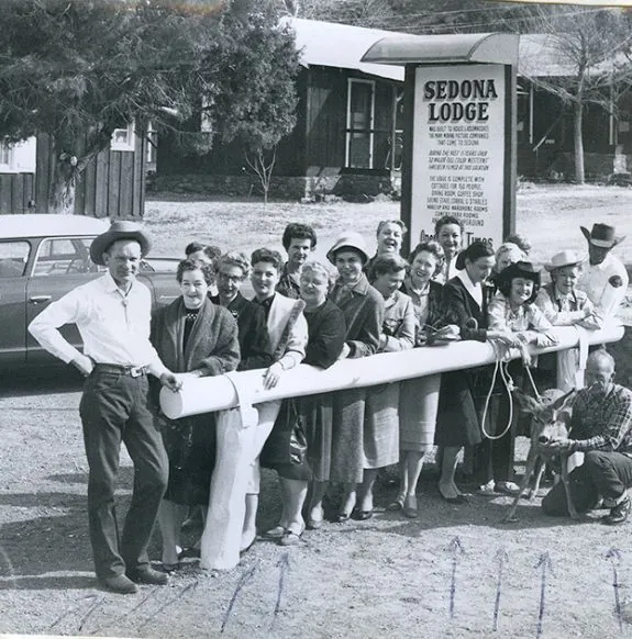 Group of people standing at wooden gate in old west attire in front of Sedona Lodge sign with antique car in background near Arabella Hotel Sedona in Sedona, AZ