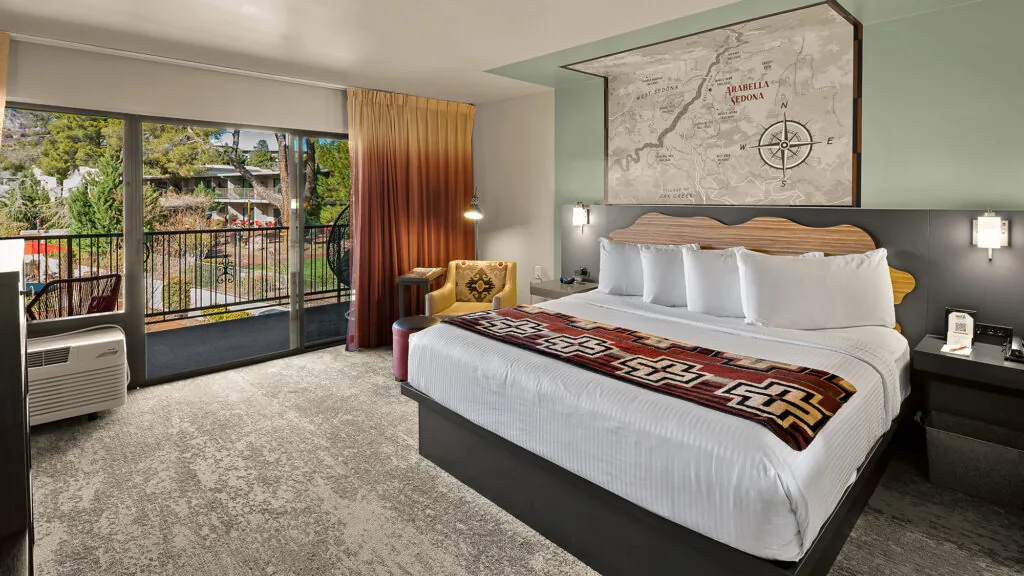 A hotel room with a large bed, desk, chair, and balcony.