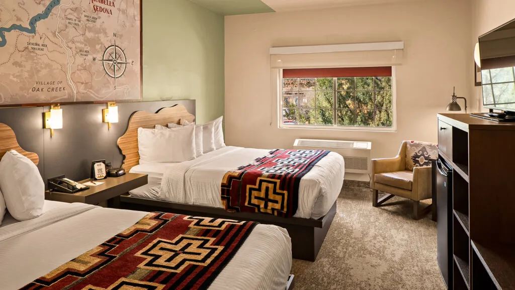 A hotel room with two beds, a window, and a flat screen TV
