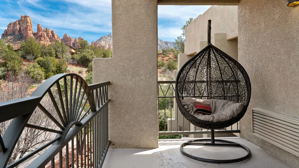 A balcony with a hanging chair and a view of red rock formations.