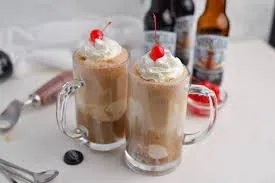 Two root beer floats at Arabella Sedona, served in clear mugs with whipped cream and a cherry, with root beer bottles and an ice cream scoop in the background.