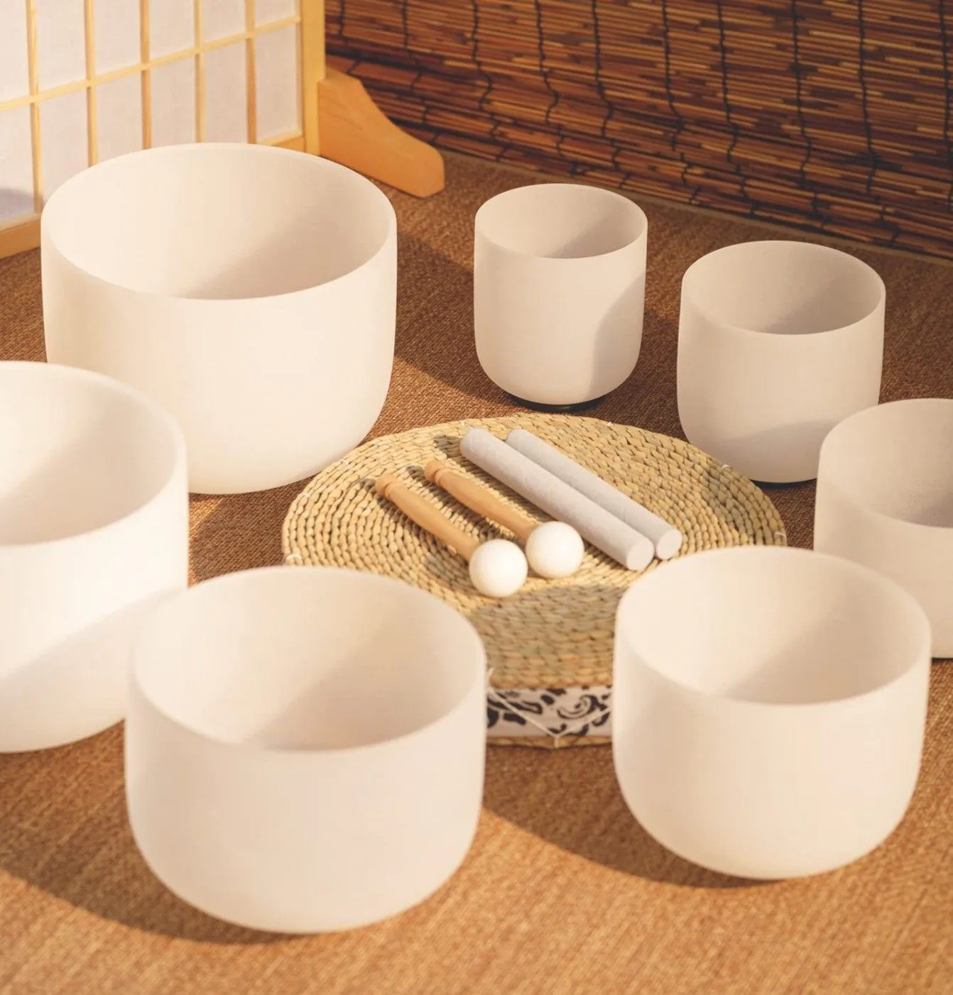 Seven white singing bowls arranged in a circle around a woven mat at Arabella Sedona, with two mallets and two strikers.